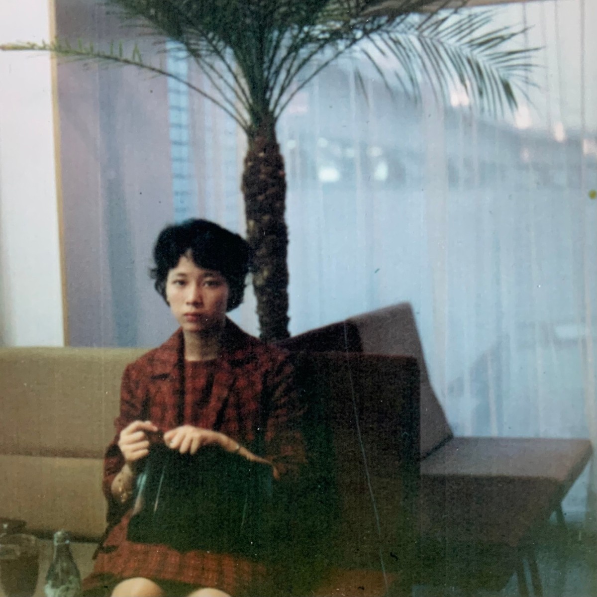 Young woman in suit jacket and dress, 1960s, seated in airport, nervously holding her purse and looking at the camera