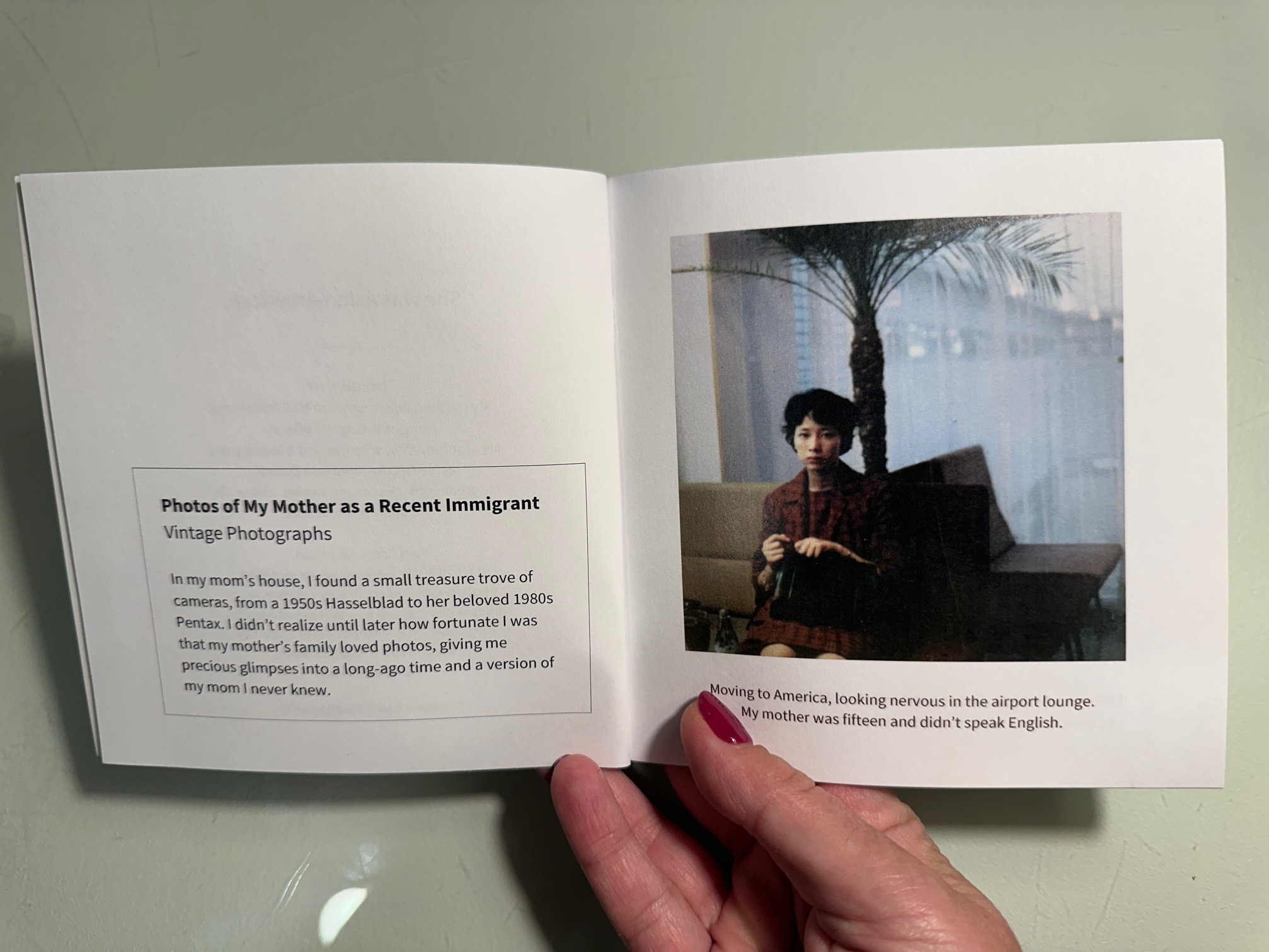 Small square book opened to show photo of a young Asian woman on the right, dressed up in the 1960s in an airport lounge, looking nervous. On the left, a description formatted to look like a museum or art gallery label: Vintage photos of my mother as a recent immigrant.