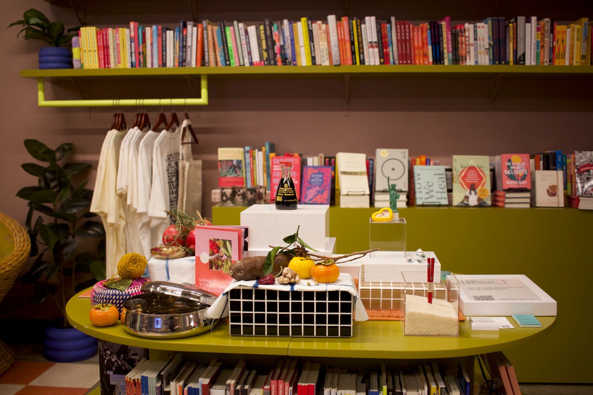 Pop-up installation by The Grief Gallery and Marigolde at bookstore Reparations Club in Los Angeles. Colorful display of books in the background. Display of items including a soy sauce bottle and fruit on a table in the foreground.